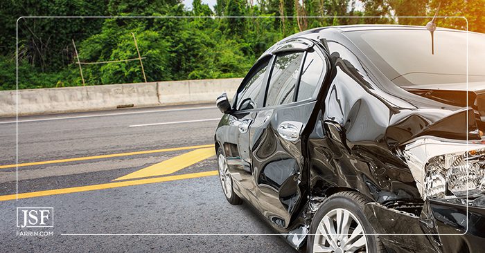 A wrecked black car on the road near a bridge barrier after a crash.
